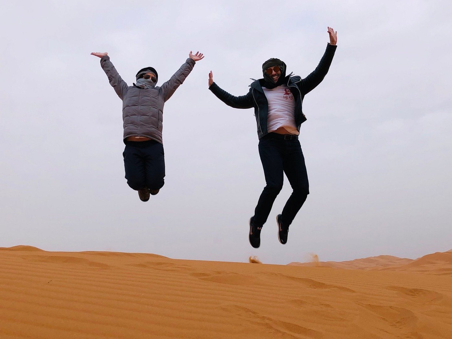Two guests jumping joyfully above a Merzouga sand dune