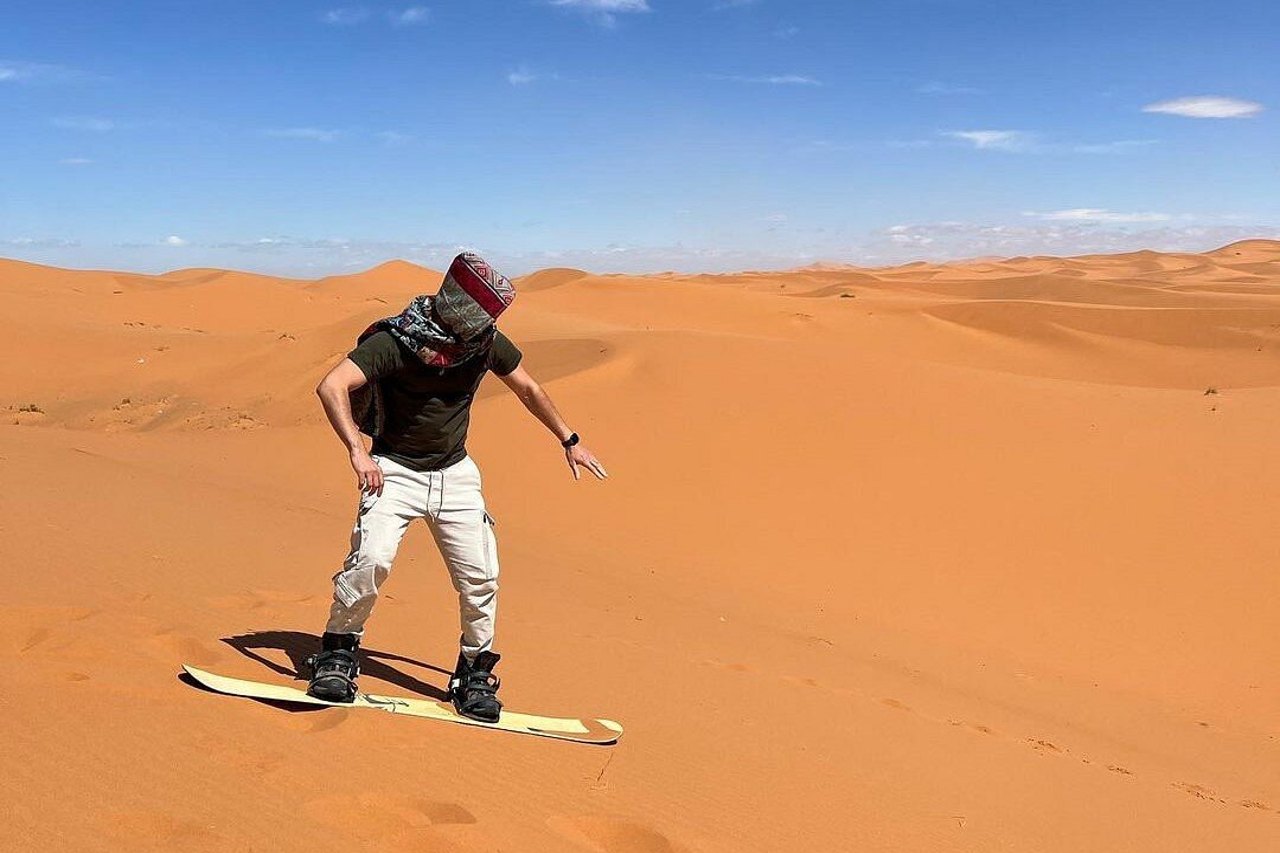 Traveler sandboarding on a golden dune in Merzouga